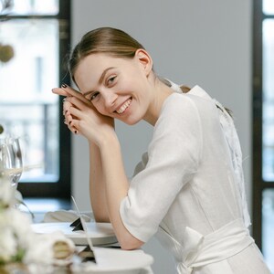 Bride in a white linen wrap dress with a bow at the back, smiling at a table