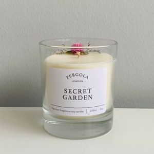 Puede incluir: Un portavelas de cristal transparente con una vela blanca. La vela tiene una etiqueta que dice "SECRET GARDEN" y est&aacute; rematada con flores secas. La vela es de 270 ml y 9 oz.