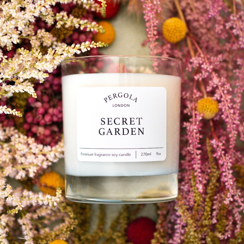 Puede incluir: Una vela de vidrio con un interior de cera blanca. La etiqueta dice "PERGOLA LONDON SECRET GARDEN". La vela est&aacute; rodeada de flores rosas y amarillas. La vela es de 270 ml.