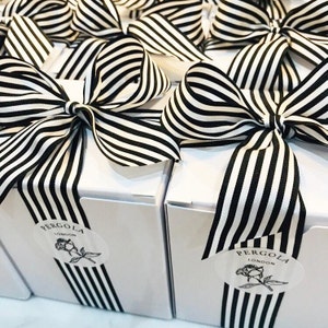 Puede incluir: Cajas de regalo blancas atadas con lazos de cinta a rayas blancas y negras. Cada caja tiene una raya de cinta a juego en la parte delantera y una etiqueta que dice "PERGOLA LONDON" con una ilustraci&oacute;n de rosa.