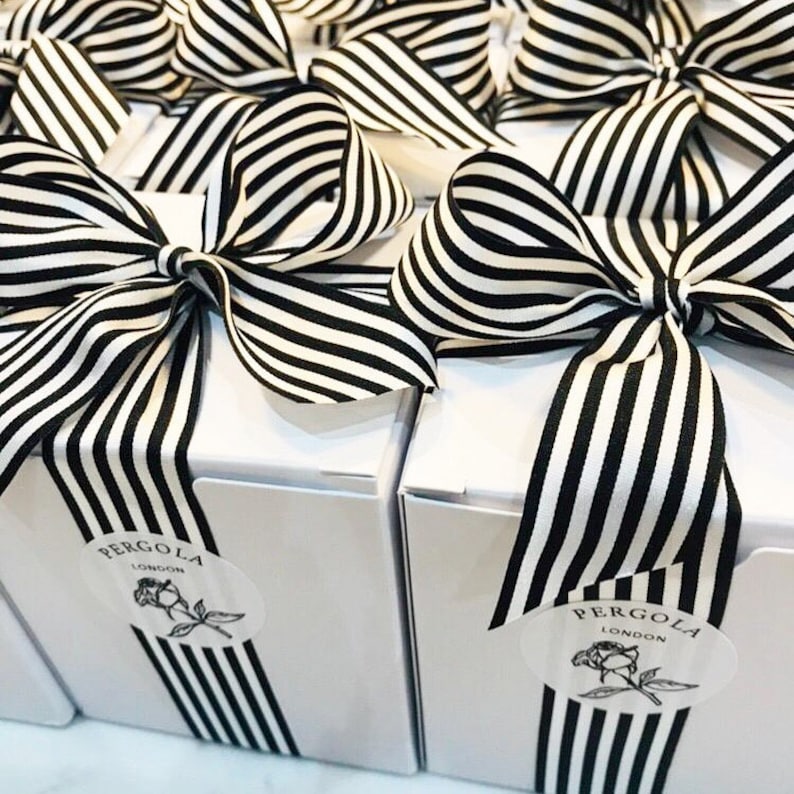 Puede incluir: Cajas de regalo blancas atadas con lazos de cinta a rayas blancas y negras. Cada caja tiene una raya de cinta a juego en la parte delantera y una etiqueta que dice "PERGOLA LONDON" con una ilustraci&oacute;n de rosa.