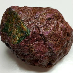 May include: A large, irregularly shaped rock with a deep purple hue and a green patch on one side. The rock has a rough, textured surface.