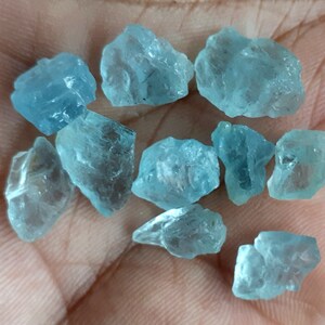 Puede incluir: Una colecci&oacute;n de diez piedras preciosas de aguamarina en bruto de varios tama&ntilde;os y formas. Las piedras son de color azul claro y tienen una apariencia transl&uacute;cida.