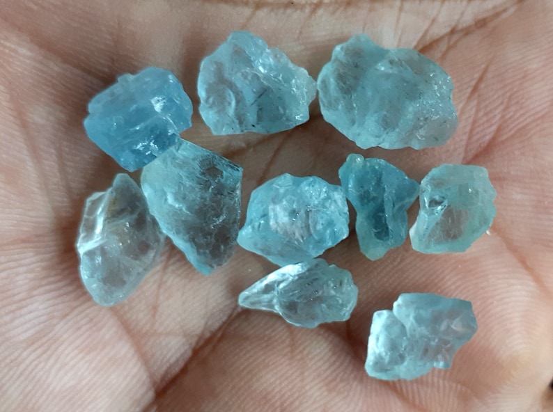 Puede incluir: Una colecci&oacute;n de diez piedras preciosas de aguamarina en bruto de varios tama&ntilde;os y formas. Las piedras son de color azul claro y tienen una apariencia transl&uacute;cida.