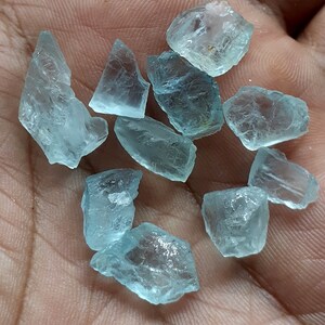 Puede incluir: Una colecci&oacute;n de diez piedras brutas de aguamarina azul claro. Las piedras son de varias formas y tama&ntilde;os, algunas tienen una apariencia m&aacute;s transl&uacute;cida que otras.