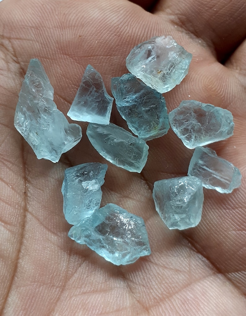 Puede incluir: Una colecci&oacute;n de diez piedras brutas de aguamarina azul claro. Las piedras son de varias formas y tama&ntilde;os, algunas tienen una apariencia m&aacute;s transl&uacute;cida que otras.
