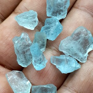 Puede incluir: Una colecci&oacute;n de diez cristales de aguamarina en bruto de diferentes tama&ntilde;os y formas. Los cristales son de color azul claro y tienen una apariencia transl&uacute;cida.