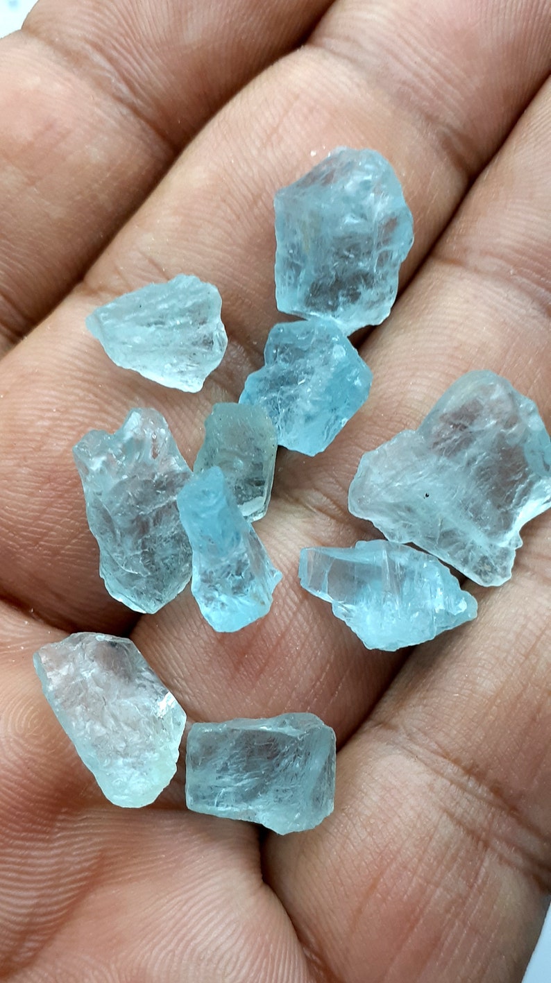 Puede incluir: Una colecci&oacute;n de diez cristales de aguamarina en bruto de diferentes tama&ntilde;os y formas. Los cristales son de color azul claro y tienen una apariencia transl&uacute;cida.