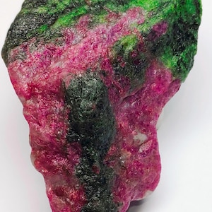以下が含まれることがあります： 鮮やかな色彩の、未加工の原石。深いマゼンタ、フォレストグリーン、チャコールグレーの印象的な組み合わせが特徴です。この自然な岩石の形状は、コレクターやジュエリーメーカーに最適です。