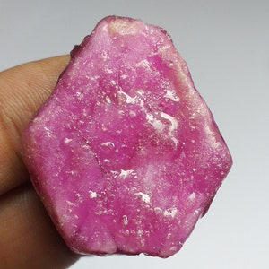 May include: A large, pink, rough-cut ruby gemstone with a smooth, polished surface.