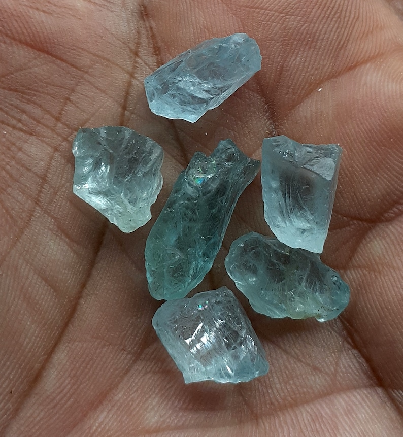 Puede incluir: Seis cristales de aguamarina en bruto de diferentes tama&ntilde;os y formas. Los cristales son transl&uacute;cidos y tienen un ligero tono verde.