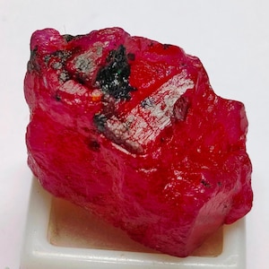Peut inclure: Une grosse pierre précieuse de rubis rouge brute avec des inclusions noires. Le rubis est d'une couleur rouge foncé et riche et a une finition naturelle non polie.
