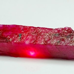 May include: A large, rough, red ruby gemstone with a deep red color. The ruby has a natural, unpolished finish.