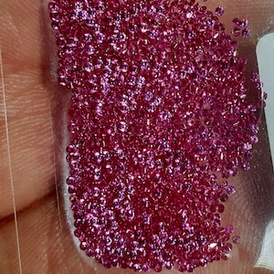 Può includere: Una vista ravvicinata di una grande quantità di piccole pietre preziose rotonde di colore rosa. Le pietre preziose sono sparse su una superficie bianca.