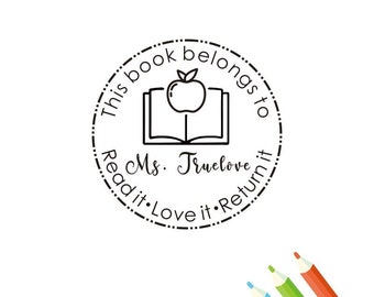 May include: A round, black and white stamp with the text "This book belongs to Ms. Truelove. Read it. Love it. Return it." An apple sits atop an open book. Colored pencils are in the bottom right corner.