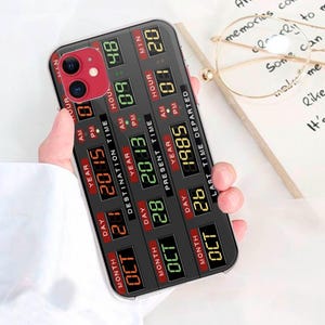 Puede incluir: Una funda de teléfono negra y roja con una pantalla digital que muestra la fecha y la hora. La pantalla muestra la fecha como 26 de octubre de 1985 y la hora como 01:20. La funda tiene un borde negro y un fondo rojo.