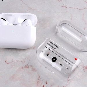 May include: A clear plastic case for Apple AirPods with a black and white design that says "Song Name" and "Artist Name" with a play button and volume controls.