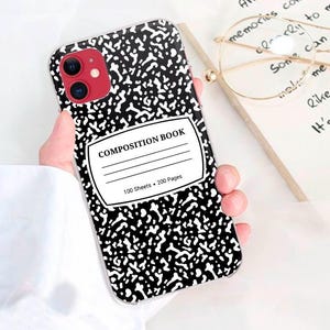 May include: A smartphone case featuring a black and white speckled pattern resembling a classic composition book cover. The center displays a white label with the text COMPOSITION BOOK, 100 Sheets, and 200 Pages printed in black ink.
