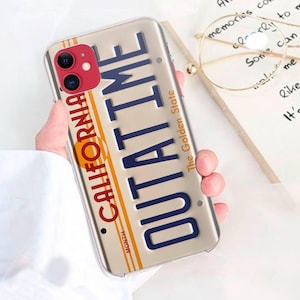 May include: A clear phone case featuring a California license plate design. The plate reads "OUTATIME" and "The Golden State". The case is decorated in red, white and blue.