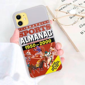 Puede incluir: Una funda transparente para teléfono con un diseño rojo, blanco y negro. La funda presenta una portada de almanaque deportivo vintage con el texto "Grays Sports Almanac 1950-2000".