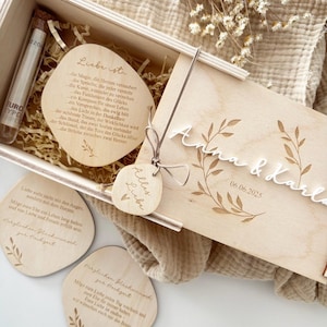 K&ouml;nnte beinhalten: Ein Holzbox-Set mit Gravurdetails, einschlie&szlig;lich eines Reagenzglases, herzf&ouml;rmigen Holzanh&auml;ngern und einem Deckel mit den Namen "Anna & Karla" und dem Datum "06.06.2025". Das Set zeigt florale Designs und deutschen Text.