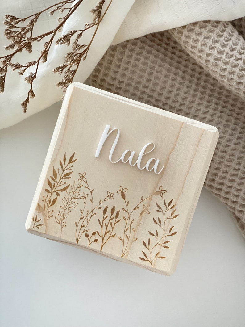 May include: A wooden block with the name "Nala" engraved in white lettering. The block has a floral design etched into the surface.