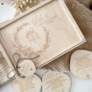 May include: A wooden gift box with a floral wreath design and the German text "Gl&uuml;ck ist dich als beste Freundin zu haben." A tag with the words "Besties for ever" is tied to the box. Three wooden coasters with German text are also visible.