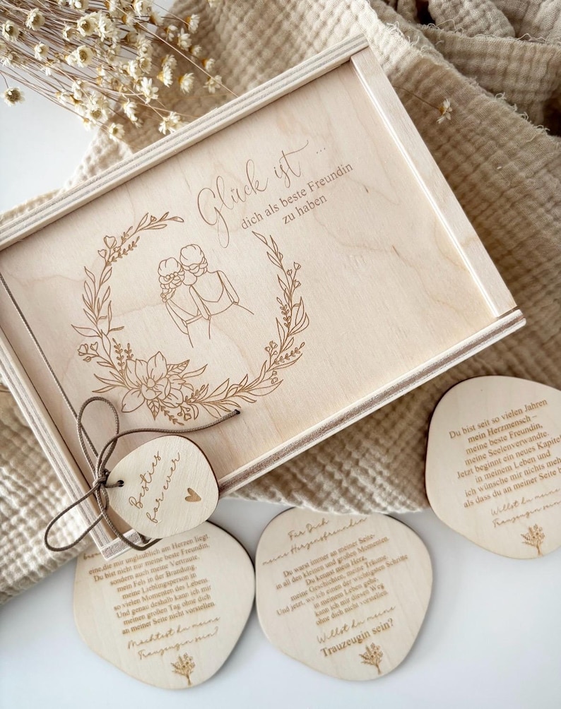 May include: A wooden gift box with a floral wreath design and the German text "Gl&uuml;ck ist dich als beste Freundin zu haben." A tag with the words "Besties for ever" is tied to the box. Three wooden coasters with German text are also visible.