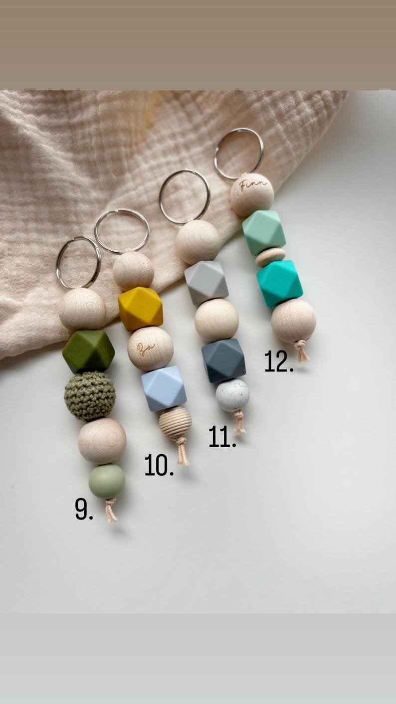 May include: Four keychains with wooden beads and colorful silicone beads. Each keychain has a silver ring. The beads are in various shapes and colors, including green, yellow, gray, and blue. Some keychains have a name engraved on a wooden bead.