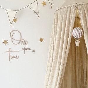 Könnte beinhalten: Ein weißes Baldachin-Zelt mit einem Heißluftballon, der von der Oberseite hängt. Das Zelt ist mit einer Lichterkette und goldenen Sternen verziert. Die Wand hinter dem Zelt hat ein Holzschild mit der Aufschrift "Es war einmal".
