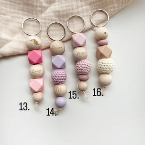 May include: Four keychains with wooden and silicone beads in various shapes and colors. Each keychain has a silver ring and is personalized with a name. One keychain features a unicorn design. Numbers 13, 14, 15, and 16 are visible.
