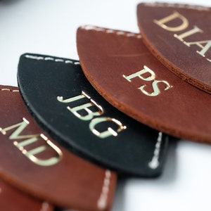 May include: Five leather tags with gold lettering. The tags are in a semi-circle shape and have the names "WJ", "MD", "JBG", "PS", and "DIANA" on them.