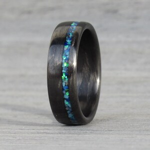 May include: A black carbon fiber ring with a thin band of blue and green opal inlay.