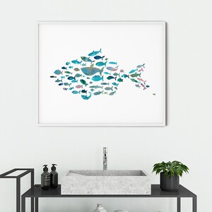 K&ouml;nnte beinhalten: Ein gerahmter Kunstdruck mit einem gro&szlig;en Fisch, der aus zahlreichen kleineren Fischen in Blau-, T&uuml;rkis- und Gr&uuml;nt&ouml;nen besteht. Das Kunstwerk wird &uuml;ber einem Waschbecken im Badezimmer ausgestellt und verleiht dem Raum ein maritimes Thema. Der Druck ist in einem wei&szlig;en Rahmen.