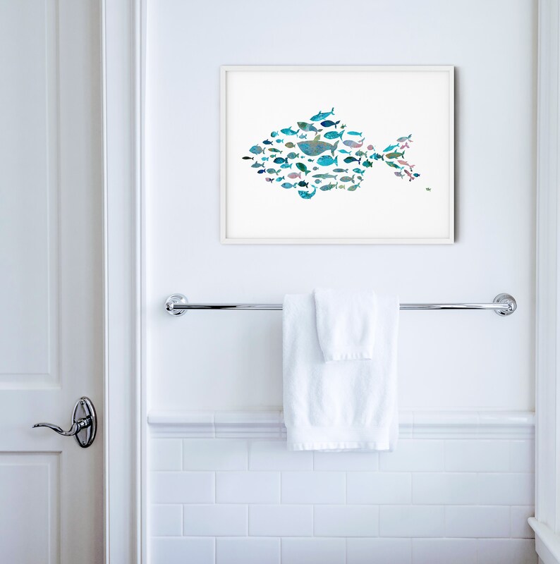 K&ouml;nnte beinhalten: Ein gerahmter Kunstdruck mit einem Fisch, der aus verschiedenen Illustrationen von blauen und t&uuml;rkisfarbenen Fischen besteht. Das Kunstwerk wird an einer wei&szlig;en Wand &uuml;ber einem Handtuchhalter aus Chrom mit einem gefalteten wei&szlig;en Handtuch gezeigt. Der Raum hat wei&szlig;e Fliesen und eine wei&szlig;e T&uuml;r.
