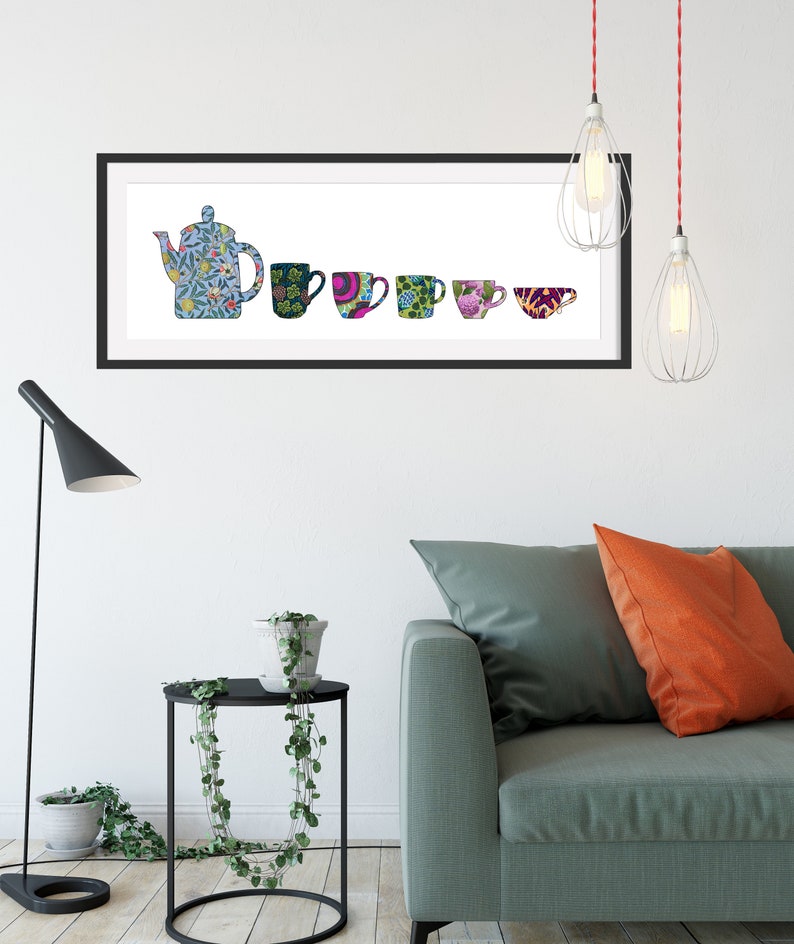 May include: A framed print of a blue teapot and five colourful mugs with floral and geometric patterns. The print is hanging on a white wall above a green sofa with orange cushions.