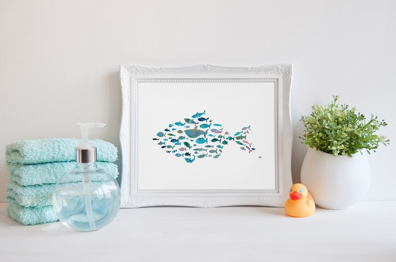 K&ouml;nnte beinhalten: Ein gerahmter Druck mit einem Fisch, der aus verschiedenen Illustrationen von blauen und t&uuml;rkisfarbenen Fischen besteht. Das Bild ist vor einem wei&szlig;en Hintergrund, mit einem Stapel t&uuml;rkisfarbener Handt&uuml;cher, einem Seifenspender, einer kleinen Pflanze und einer Gummiente.