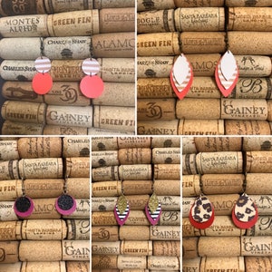 May include: Four pairs of earrings displayed on a cork background. The earrings are made of leather and feature various patterns, including stripes, polka dots, animal print, and geometric designs. The earrings are in shades of red, pink, black, white, and gold.