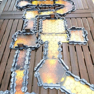 May include: A set of gray stone dungeon tiles for a tabletop role-playing game. The tiles are arranged in a winding path with a central room. The tiles are made of a thick cardboard with a printed image of stone walls and a dungeon floor.