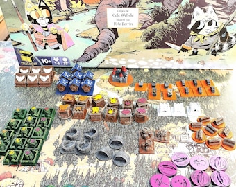 Op de afbeelding: Een bordspel genaamd "ROOT: Conflit dans les Sous-Bois" met verschillende spelonderdelen, waaronder houten gebouwen, tokens en miniatuurfiguren. De speldoos heeft een cartoonillustratie van een kat en een wasbeer.