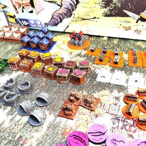 May include: A collection of colorful wooden game pieces, including houses, trees, and other structures. The pieces are arranged on a table with a brown background. The game pieces are made of wood and painted in various colors, including red, blue, green, yellow, and brown.