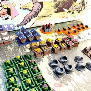May include: A collection of colorful wooden game pieces for a board game. The pieces include houses, castles, and other structures. The pieces are made of wood and painted in various colors, including blue, green, yellow, red, and brown. The pieces are arranged on a table, and there are several other game pieces in the background.