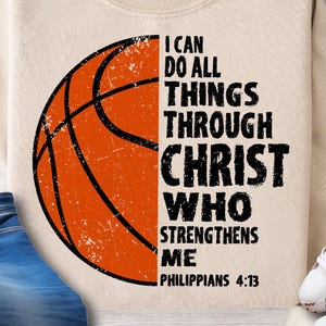 Puede incluir: Sudadera crema con un gráfico de baloncesto y el texto "Todo lo puedo en Cristo que me fortalece, Filipenses 4:13." Se ven también unos vaqueros azules y zapatillas blancas.