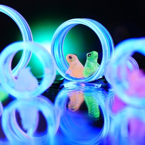 May include: Multiple glowing blue circular rings arranged in a cluster, each framing a small, colourful figurine. The figurines include orange, green, white, and pink creatures, all positioned within the centre of the illuminated rings.