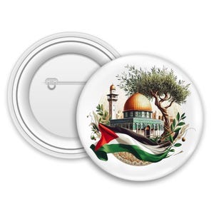 Op de afbeelding: Een witte button met een gedetailleerde illustratie van de Rotskoepel, een olijfboom en de Palestijnse vlag. De button heeft een veiligheidsspeld op de achterkant.