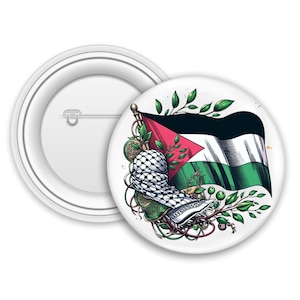 Op de afbeelding: Een witte button met een illustratie van de Palestijnse vlag, een keffiyeh en groene bladeren. De button is rond en heeft een veiligheidsspeld aan de achterkant. Een andere button wordt apart getoond.