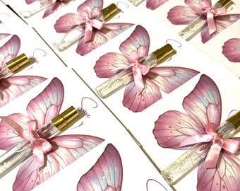 Può includere: Disposizione di bottiglie di profumo a tema farfalla. Ogni bottiglia è abbinata a un'illustrazione di farfalla rosa su una carta bianca. Le ali della farfalla sono rosa e viola, con una bottiglia di profumo dorata e un nastro rosa.