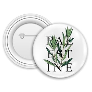 Op de afbeelding: Witte ronde badge met het woord "PALESTINE" in zwarte hoofdletters, overlegd met een groen olijftakontwerp. De badge is rond en heeft een speld op de achterkant.