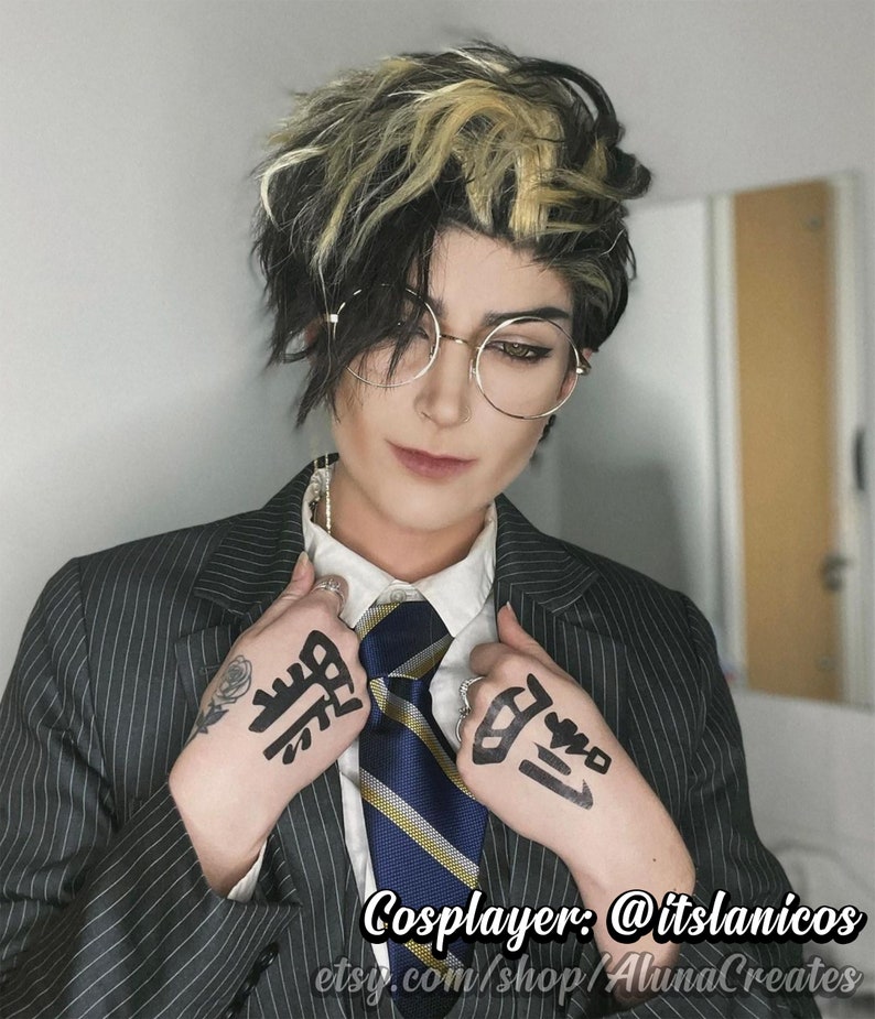 May include: A person wearing a black and white striped suit jacket with a white collared shirt and a blue and yellow striped tie. The person has black and blonde hair and is wearing round glasses. The person has black ink markings on both hands. The text "Cosplayer: @itslanicos etsy.com/shop/AlunaCreates" is visible at the bottom of the image.