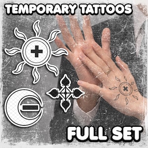 May include: Temporary tattoo set featuring sun, moon, and cross designs, with the text "TEMPORARY TATTOOS" and "FULL SET". The image shows a hand with a sun tattoo. The tattoos are black and white.